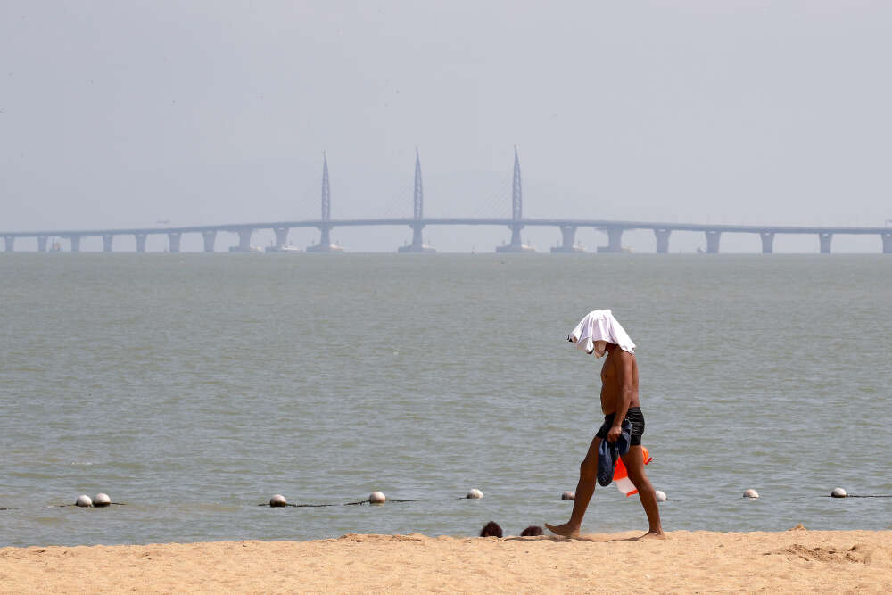 Une homme marche sur une plage de laquelle on voit le pont qui sâ€™Ã©tend sur 55 kilomÃ¨tres au dessus du delta de la riviÃ¨re des Perles, le 22 octobre.