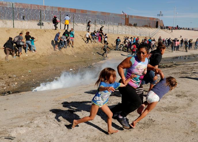 Migrants flee the gas sent to prevent them from crossing the US border in Tijuana, Mexico, on 25 November.