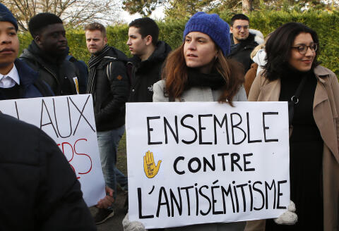 Students holding a placard reading "Together against Anti-Semitism" take part of a ceremony in tribute to Ilan Halimi at a makeshift memorial, in Sainte Genevieve des Bois, south suburb of Paris, Wednesday, Feb. 13, 2019, two days after two trees planted in memory of the 23-year-old Jewish man abducted and killed over a decade ago, have been found vandalised. (AP Photo/Francois Mori)