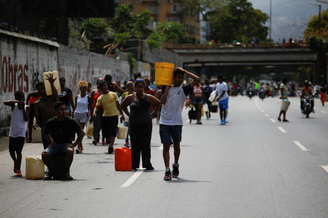 Des Vénezueliens marchent sur une autoroute, transportant des conteneurs d’eau recueillie dans un égout, à Caracas, le 11 mars 2019.