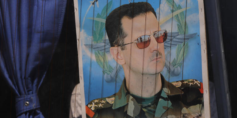 FILE - In this Aug. 13, 2018 file photo, a Syrian refugee holds a poster of President Bashar Assad in a bus window at the border crossing point of Jdedeh Yabous, on his way to Syria. Assad said Sunday, Feb. 17, 2019, that only the Syrian army can protect groups in northern Syria. In a speech in the Syrian capital Damascus on Sunday, he appeared to be referring to U.S.-allied Kurdish groups, which fear a Turkish assault once American troops withdraw from northeastern Syria. (AP Photo/Sergei Grits, File)