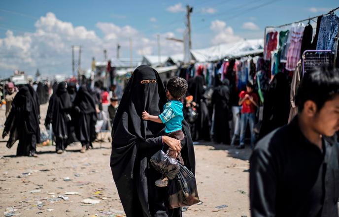Une femme déplacée de la province de Deir ez-Zor, dans l’est de la Syrie, porte un enfant alors qu’elle se promène dans le camp de personnes déplacées d’Al-Hol, dans le gouvernorat d’Al-Hasakeh, dans le nord-est de la Syrie, le 18 avril 2019. Délogées lors d’une dernière offensive menée par une force terrestre dirigée par les Kurdes et des frappes aériennes de la coalition, des milliers d’épouses et d’enfants de combattants de l’Est ont envahi un groupe de villages syriens au sud du camp d’Al-Hol au cours des derniers mois. Parmi les nombreux Syriens et Irakiens, quelque 9 000 étrangers sont détenus dans une section clôturée du campement, sous la surveillance des forces kurdes.