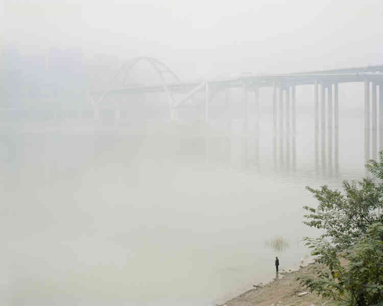 « La ville de Chongqing, par sa topographie, est en quasi permanence couverte d’un épais brouillard, d’humidité et de pollution. Cela en fait une des métropoles les moins ensoleillées du pays. Le long des berges du Yangzi Jiang, restées sauvages en de nombreux points, des pêcheurs s’adonnent à leur occupation malgré la forte pollution des eaux. Depuis 2015, le gouvernement a décidé la mise en place d’une politique de sauvegarde de l’environnement fluvial. »