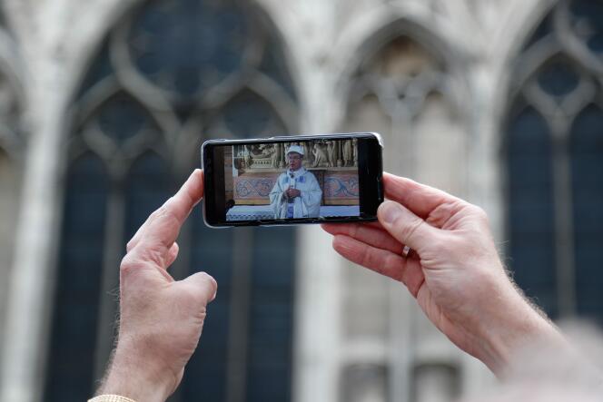 Un homme porte un smartphone montrant en direct la messe de l’archevêque de Paris, Michel Aupetit, devant la cathédrale Notre-Dame, le 15 juin, deux mois après l’incendie.