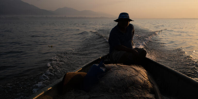 A fisherman who prefers to remain anonymous due to fear of being criminalized, rides his boat at dawn on Lake Izabal. El Estor, Izabal, Guatemala. April 1, 2019.