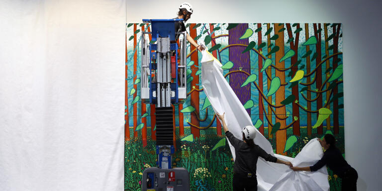 Workers remove the protections as renowned British painter David Hockney poses during the unveiling of a huge painting he is donating to the Pompidou Center in Paris, 
