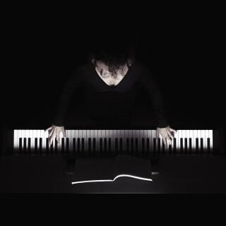 Woman playing the piano, white keys and hands on black background, overhead view in dramatic light