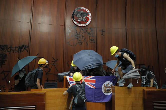 Des manifestants brandissent un drapeau colonial hongkongais et défigurent le logo de HongKong à la chambre législative, le 1er juillet.