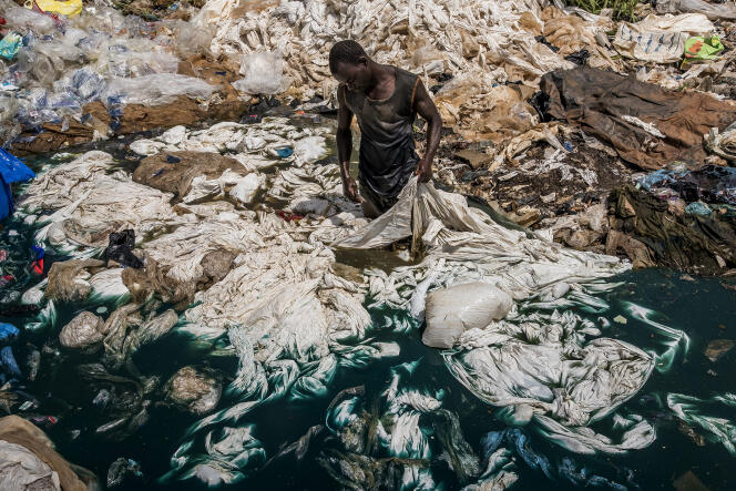 A Katabi, en Ouganda, dans une décharge située dans un marécage, un homme nettoie des sacs en plastique dont le colorant bleu va contaminer l’eau du lac Victoria.