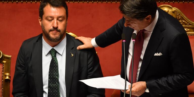 TOPSHOT - Italian Prime Minister Giuseppe Conte (R) touches Deputy Prime Minister and Interior Minister Matteo Salvini's shoulder as he delivers a speech at the Italian Senate, in Rome, on August 20, 2019, as the country faces a political crisis. Italy's Premier Conte says to offer resignation during his speech at the Senate after calling Italy's far-right Interior Minister Matteo Salvini 