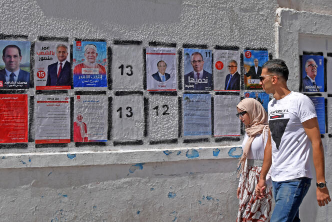 Un couple de jeunes Tunisiens passe devant les portraits des candidats du premier tour de l’élection présidentielle, à Tunis, le 7 septembre.