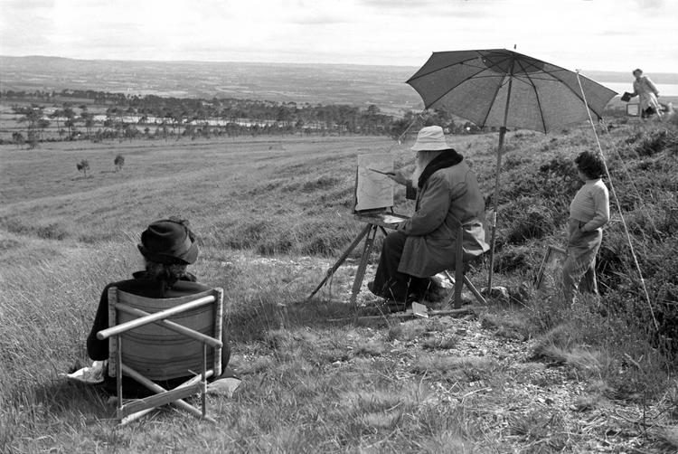 « J’ai redécouvert cette photographie à l’occasion de ce travail de recherche sur la Bretagne des années 1950. Retrouverait-on encore aujourd’hui une telle scène ? Le peintre installé avec son chevalet, son parasol et sa femme qui attend patiemment le chef-d’œuvre achevé ».