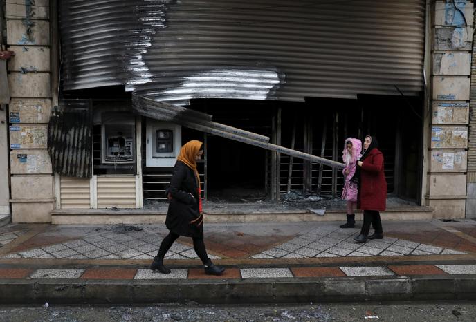 Des piétons passent devant une banque incendiée lors des manifestations à Téhéran, le 20 novembre.