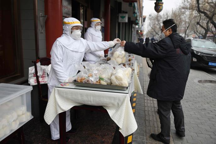Un restaurateur portant des vêtements de protection contre le coronavirus sert un client dans la rue, à Pékin, le 20 février.