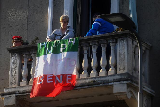 Une femme installe un drapeau italien sur lequel on peut lire « tout ira bien » sur son balcon à Milan, le 16 mars.