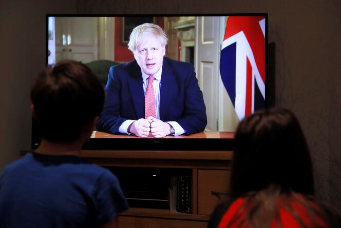 Deux enfants regardent à la télévision la conférence de presse de Boris Johnson alors que la propagation du Covid-19 se poursuit à Hertford, en Grande-Bretagne, le 23 mars 2020.