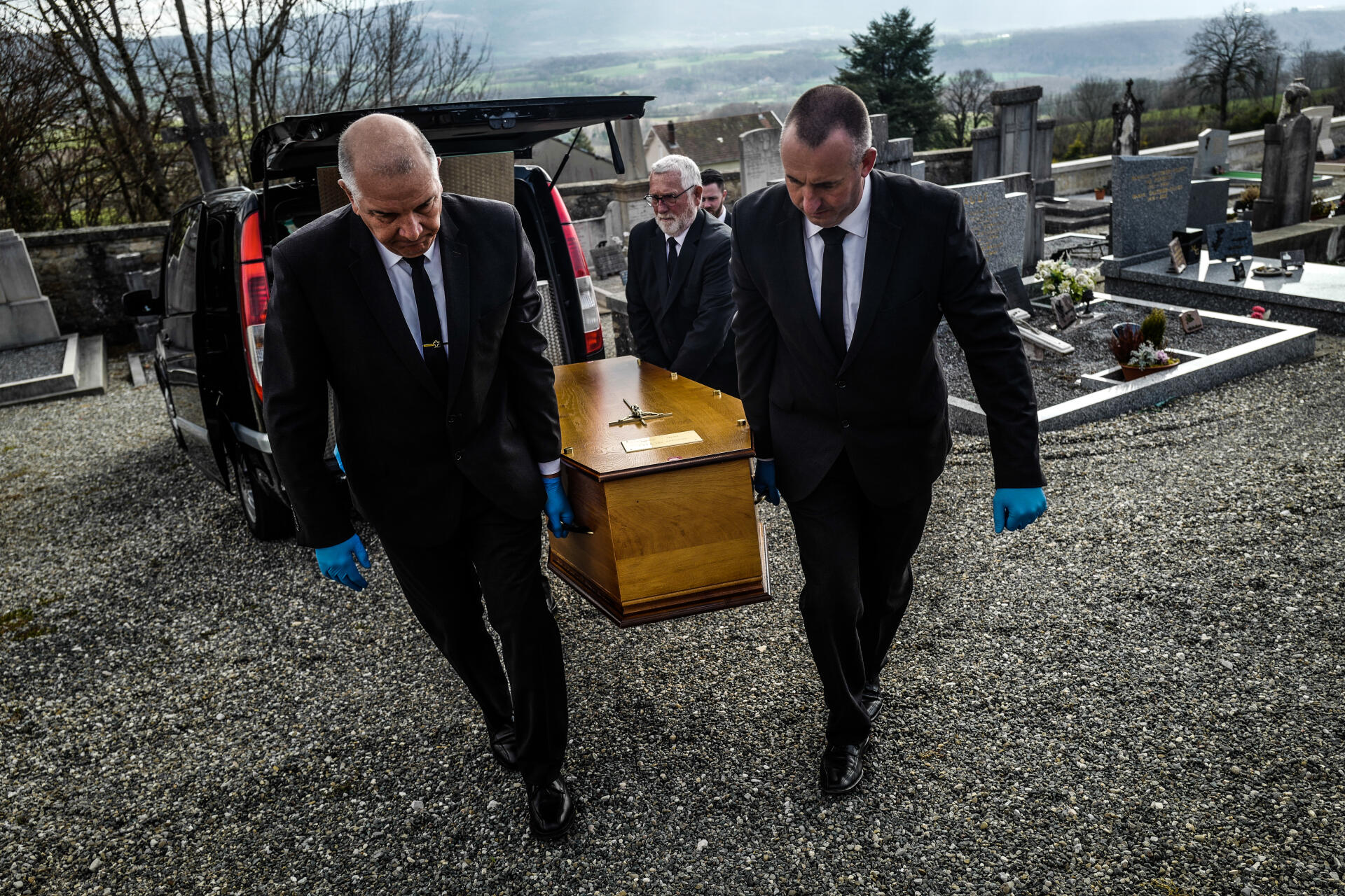 Les mains gantées de caoutchouc, les employés des pompes funèbres saisissent le cercueil par les poignées pour ne pas avoir de contact avec le bois.