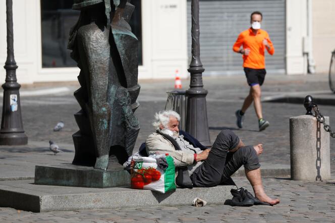 Un joggeur, portant un masque de protection, passe à côté d’un sans-abri dans une rue de Paris, le 27 mars.