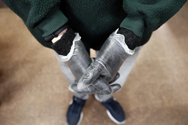 Un bénévole de Utopia56 porte des gants de protection en vinyle par dessus des gants en laine.