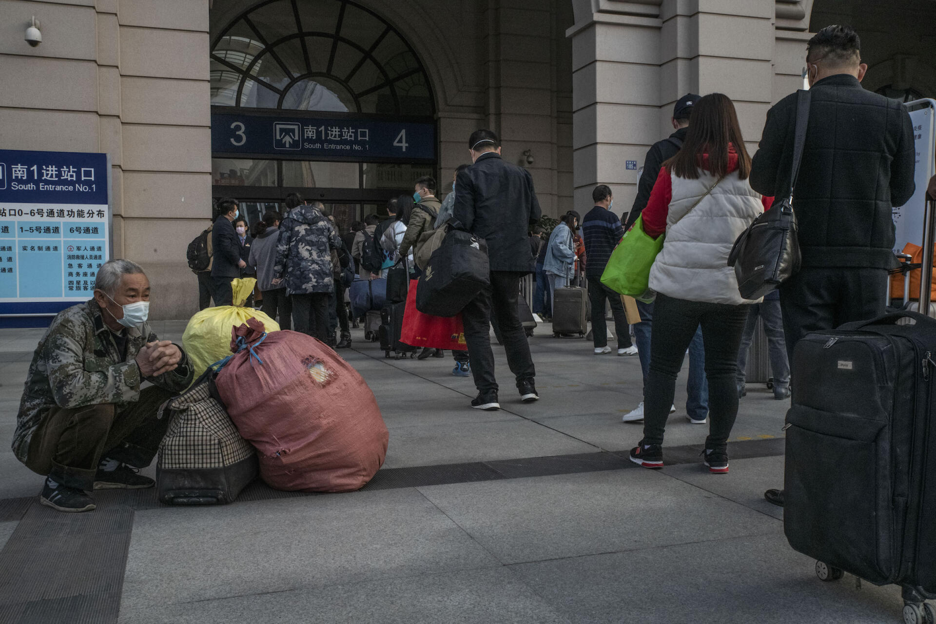 Un voyageur attend avec ses bagages pendant que d’autres rentrent dans la gare, le 8 avril à Wuhan.