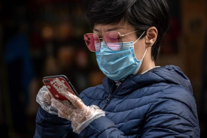 Une femme, masquée et gantée, consulte son smartphone, à Pékin, le 9 avril.