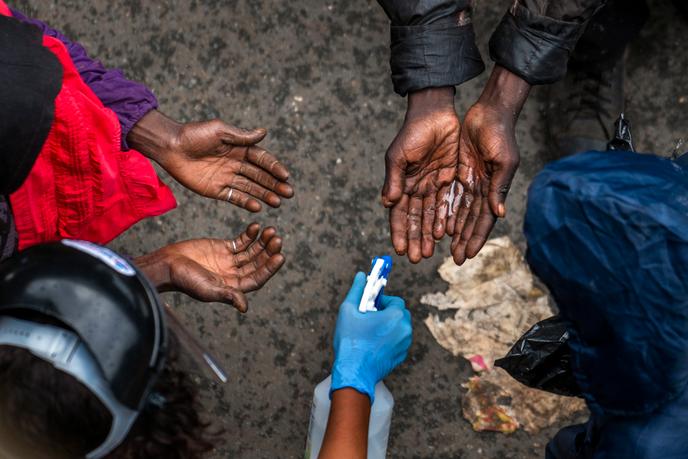 Des sans-abri qui attendent de recevoir des paniers de nourriture de donateurs privés se font désinfecter les mains le 13 avril 2020 dans le centre-ville de Johannesburg.