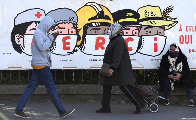 Des passants devant une affiche en hommage aux professions exposées en periode de confinement, à Paris, le 14 avril.
