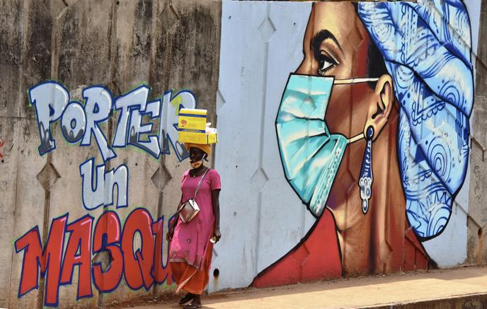 Une femme passe devant une fresque murale sensibilisant aux gestes barrières anti-coronavirus, à Conakry, en Guinée, le 4 mai 2020.