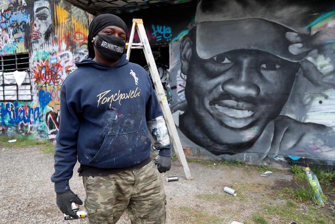 L’artiste Theo Ponchaveli devant la peinture murale qu’il a réalisée à l’image d’Ahmaud Arbery, à Dallas (Texas), le 8 mai 2020. Il porte un masque qu’il a lui-même confectionné sur lequel on peut lire « Runwithmaud ».