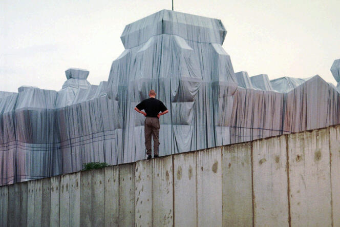 Un homme se tient sur un vestige du mur de Berlin, devant l’oeuvre de Christo « L’empaquetage du Reichstag », le 22 juin 1995.