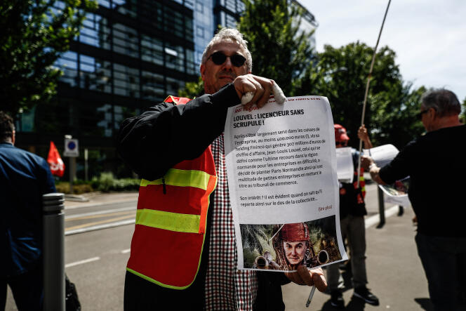 Un syndicaliste tient une affiche dénonçant les pratiques supposées de Jean-Louis Louvel, devant le tribunal de commerce de Rouen, mardi 9 juin, en pleine procédure de rachat du quotidien « Paris-Normandie ».