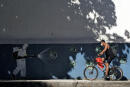 A man rides a bike in front of a mural depicting a man in protective suit spraying disinfectant, at the Tijuca neighborhood in Rio de Janeiro, Brazil on July 8, 2020, amid the new coronavirus pandemic. Brazilian President Jair Bolsonaro has tested positive for the coronavirus after months of downplaying the dangers of the disease. / AFP / MAURO PIMENTEL 