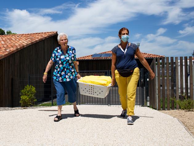 Les « villageois » sont incités à participer à l’intendance de leur « maisonnée ». Accompagnée par la « maîtresse de maison », une résidente porte un panier de linge propre.