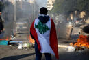 (FILES) In this file photo taken on January 14, 2020, a Lebanese anti-government protester, wrapped in a national flag, stands in front of a road blocked with burning tyres and overtunrned garbage dumpsteres in Beirut. - For months, Lebanon has grappled with its worst economic crisis since the 1975-1990 civil war.
Tens of thousands have lost their jobs or part of their salaries, while a crippling dollar shortage has sparked rapid inflation. (Photo by PATRICK BAZ / AFP)