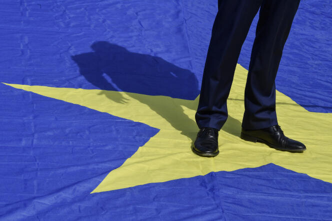 Le commissaire européen à la justice, Didier Reynders, est debout sur le drapeau européen, à Bruxelles le 9 mai 2020.