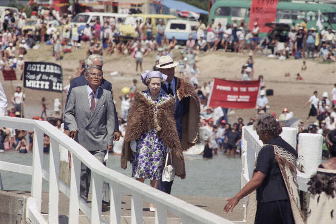 La reine d’Angleterre, Elizabeth II, et le duc d’Edinbourg arrivent à Waitangi, le 6 février 1990, pour fêter l’anniversaire des 150 ans du traité de Waitangi. Derrière eux, des Maoris manifestent.
