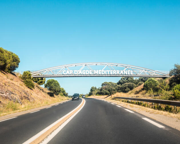 Au-dessus de la RD 612 est annoncée l'entrée au Cap d'Agde, adossée à une passerelle créée dans le cadre du chantier d'extension du golf international.