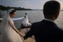 This photo taken on August 5, 2020 shows couples posing for wedding photographers next to East Lake in Wuhan in China’s central Hubei province. The city's convalescence since a 76-day quarantine was lifted in April has brought life and gridlocked traffic back onto its streets, even as residents struggle to find their feet again. Long lines of customers now stretch outside breakfast stands, a far cry from the terrified crowds who queued at city hospitals in the first weeks after a city-wide lockdown was imposed in late January to curb the spread of the COVID-19 coronavirus. / AFP / Hector RETAMAL
