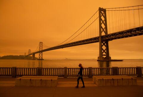 A woman walks along The Embarcadero under an orange smoke-filled sky in San Francisco, California on September 9, 2020. More than 300,000 acres are burning across the northwestern state including 35 major wildfires, with at least five towns "substantially destroyed" and mass evacuations taking place. / AFP / Brittany Hosea-Small 