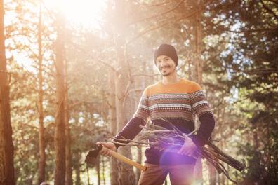 Portrait of happy young man with axe and firewood in forest
