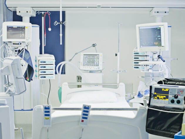 Un lit d’un service de réanimation équipé d’un électrocardioscope et de pousse-seringues.