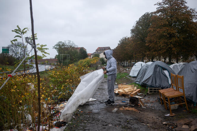 Un jeune homme tente de récupérer ce qu'il peut d'une bâche en plastique abandonnée afin de se protéger de la pluie, le 2 novembre en bordure de canal, à Saint-Denis (Seine-Saint-Denis).
