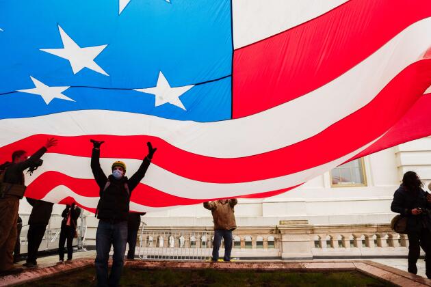Un groupe de partisans du président Trump sous un drapeau américain géant, près du Capitole.