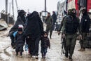 A veiled woman walks with children next to a member of the Syrian Kurdish internal security services known as Asayish, during the release of persons suspected of being related to Islamic State (IS) group fighters from the Kurdish-run al-Hol camp in Hasakeh governorate in northeastern Syria, on January 19, 2021. (Photo by Delil SOULEIMAN / AFP)