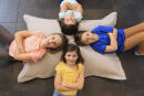 Quatre enfants disposés en étoile sur un grand coussin au sol.