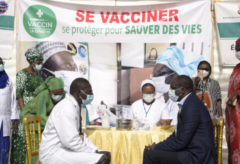 The Minister of Health and Social Action, Ablaye Diouf Sarr (R) sits in front of an health worker and gets prepared to be vaccinated - as the first one in Senegal - during the official launch of the vaccination campaign against the Covid-19, in Dakar, on February 23, 2021, as a banner is reading 'get vaccinated - protect yourself to save lives' in the background. (Photo by Seyllou / AFP)