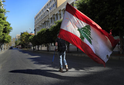 A protester holds a Lebanese flag, as he walks on a blocked main road that leads to the Central Bank during a protest against the increase in prices of consumer goods and the crash of the local currency, in Beirut, Lebanon, Tuesday, March 16, 2021. Scattered protests broke out on Tuesday in different parts of the country after the Lebanese pound hit a new record low against the dollar on the black market. (AP Photo/Hussein Malla)