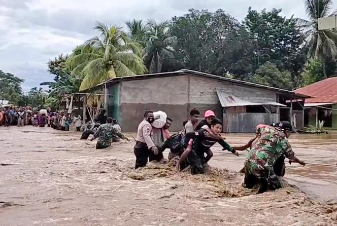 Sur cette image tirée d’une vidéo, des soldats et des policiers aident les habitants à traverser une route inondée à Malaka Tengah, en Indonésie, le 5 avril.