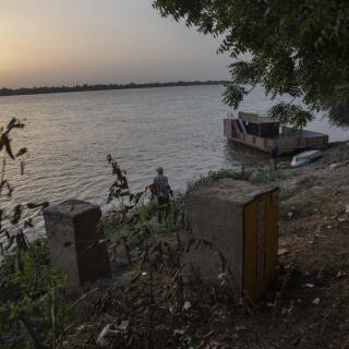 Le soleil se couche sur les rives du Nil à Atbara. Autrefois, ce bac permettait de franchir la rivière, aujourd’hui il rouille sur les flots. Un pont a été construit, il enjambe le fleuve et relie la ville à un quartier industriel où trône les usines de ciment.