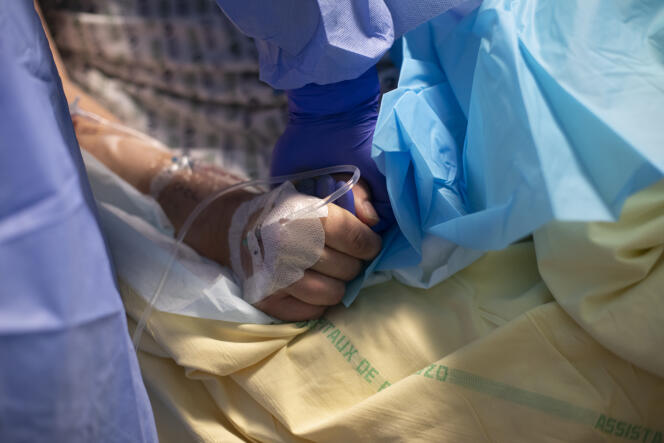 Un interne tient la main d’un patient atteint du Covid-19 pendant qu’on lui pose un cathéter artériel, à l’Hôpital Bichat, à Paris, le 8 avril.